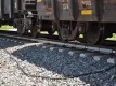Freight train wheels and bogies passing over railway track equipped with WILD IV monitoring sensors on concrete sleepers, with ballast stones and connecting cables visible beneath the train.