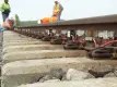 Railway workers in high-visibility safety gear installing WILD IV monitoring equipment on railroad tracks, with multiple L.B. Foster sensor units and red cables visible along the rail sections, concrete sleepers and ballast stones in foreground.